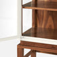 Close-up of the Made Goods Jamison Cabinet with a partially open glass-paneled door, showcasing two interior shelves and elegant walnut legs against a plain background.