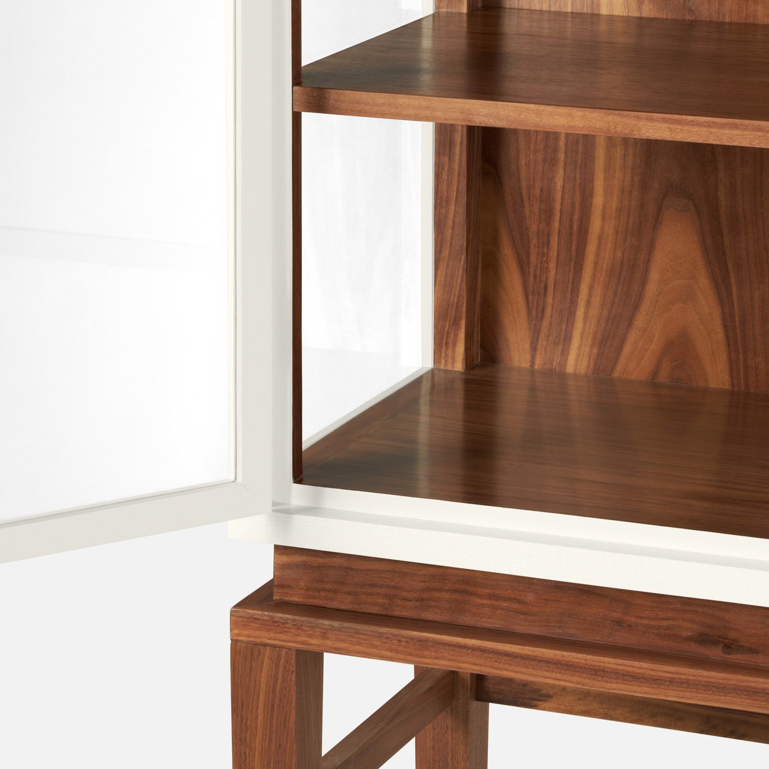 Close-up of the Made Goods Jamison Cabinet with a partially open glass-paneled door, showcasing two interior shelves and elegant walnut legs against a plain background.