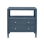 The Jarin Nightstand Collection by Made Goods features a dark blue wooden nightstand with two drawers, European glides, brass knobs, an open shelf, and four tapered legs. Shown against a white background.