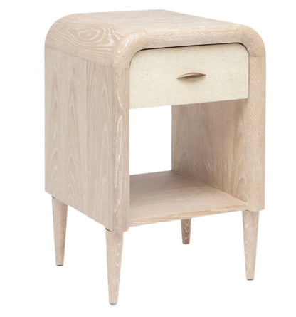 The Pierre Nightstand Collection by Made Goods features a light wood nightstand with a rounded frame, single drawer with a small handle, and an open lower shelf.