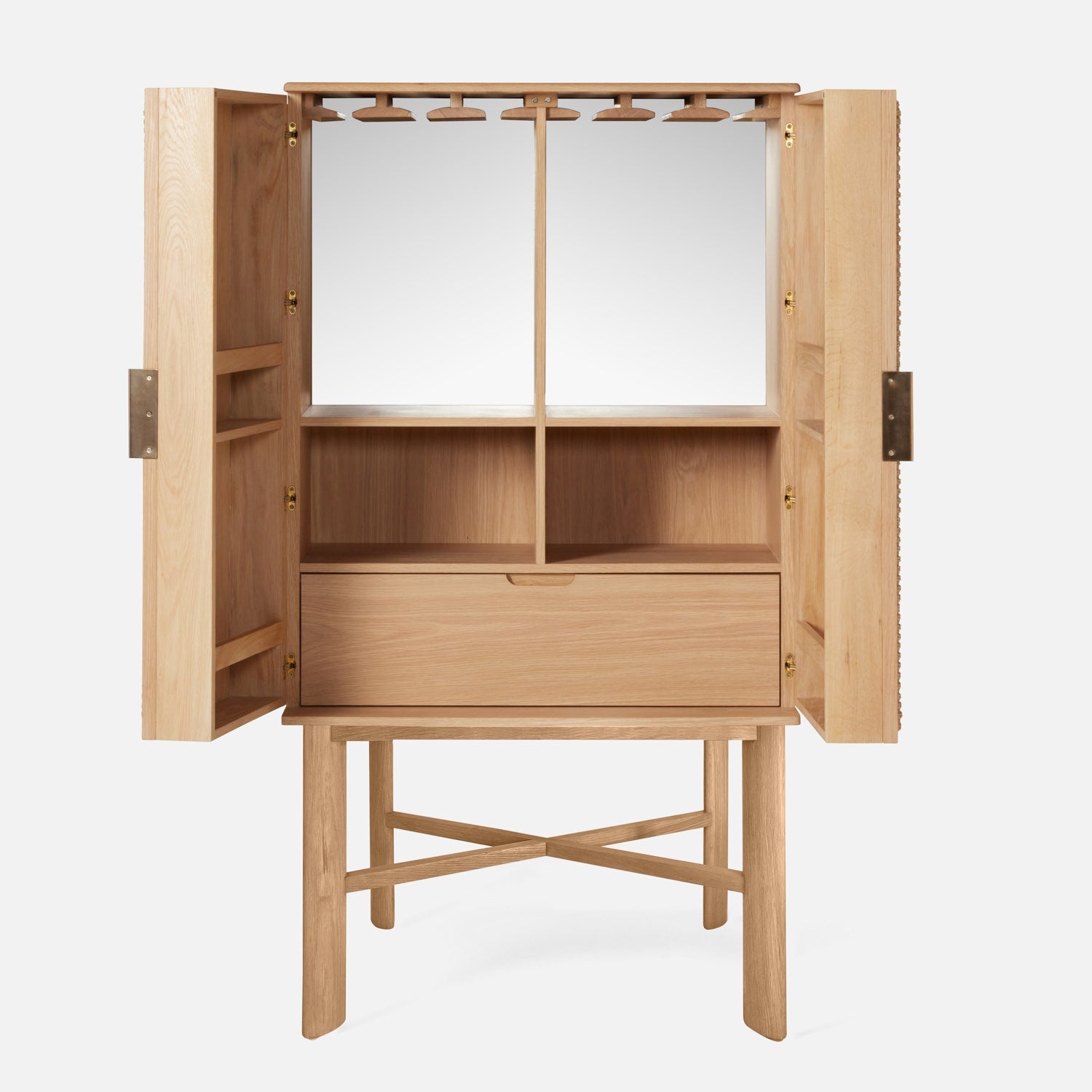 The Vanna Bar Cabinet by Made Goods features open doors that reveal shelves, a drawer, a mirrored back, and hanging hooks, all supported by a matching wood stand with crossbar legs in an elegant oak veneer.