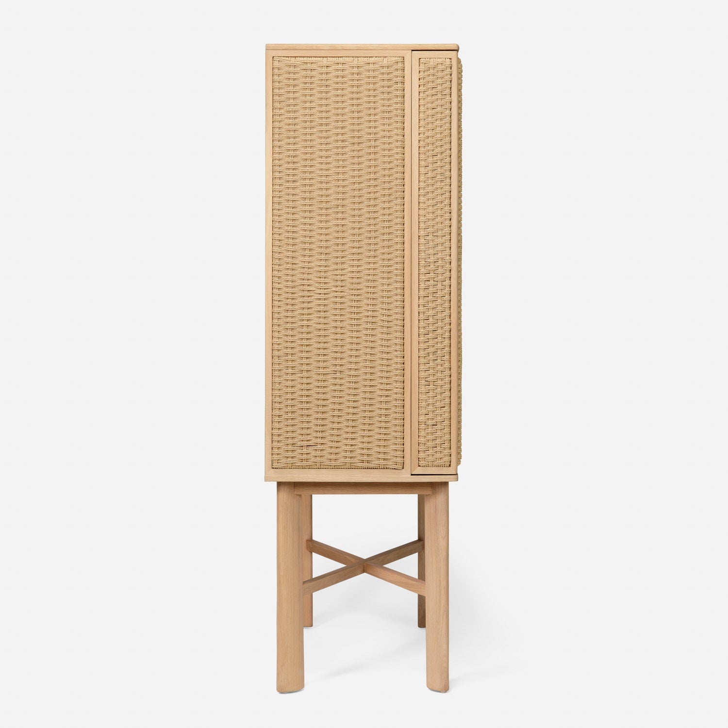 The Vanna Bar Cabinet by Made Goods features tall oak veneer construction and two woven rattan doors, standing on four legs with cross supports, shown against a plain white background.