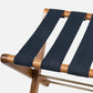 Close-up of the Made Goods Walvia Teak and Navy Luggage Rack featuring three wide navy canvas straps across a teak frame, set against a plain white background.
