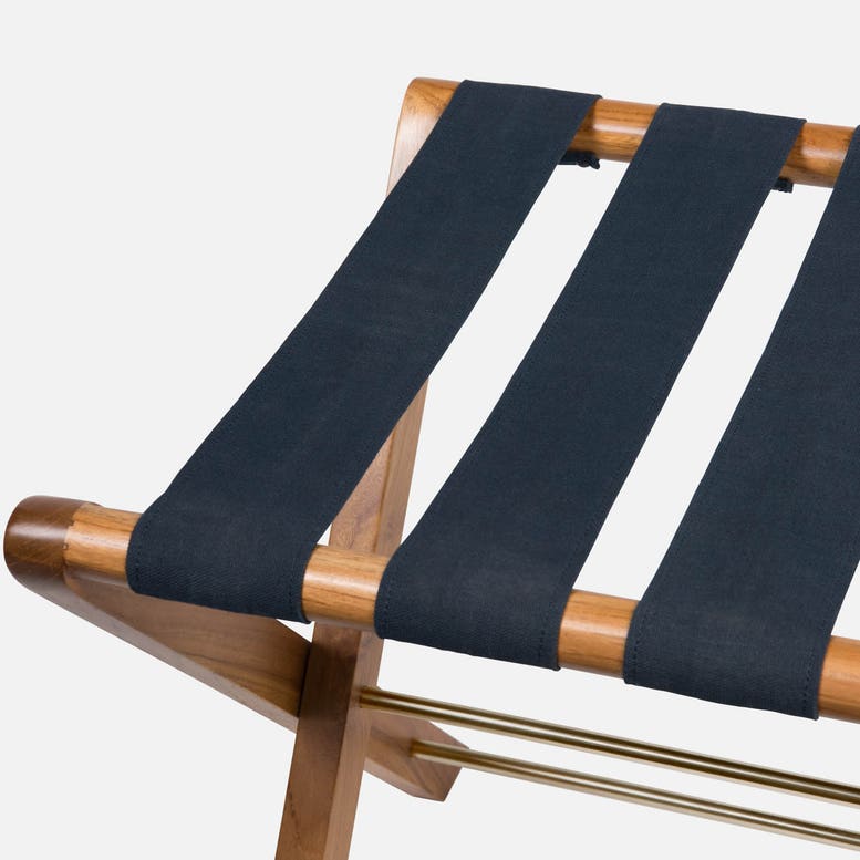Close-up of the Made Goods Walvia Teak and Navy Luggage Rack featuring three wide navy canvas straps across a teak frame, set against a plain white background.