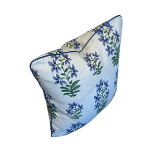 The Shani Blue Pillow by HIVE ALTERATIONS features a white background with a blue and green floral pattern, accented by blue piping—expertly crafted for a luxurious touch.
