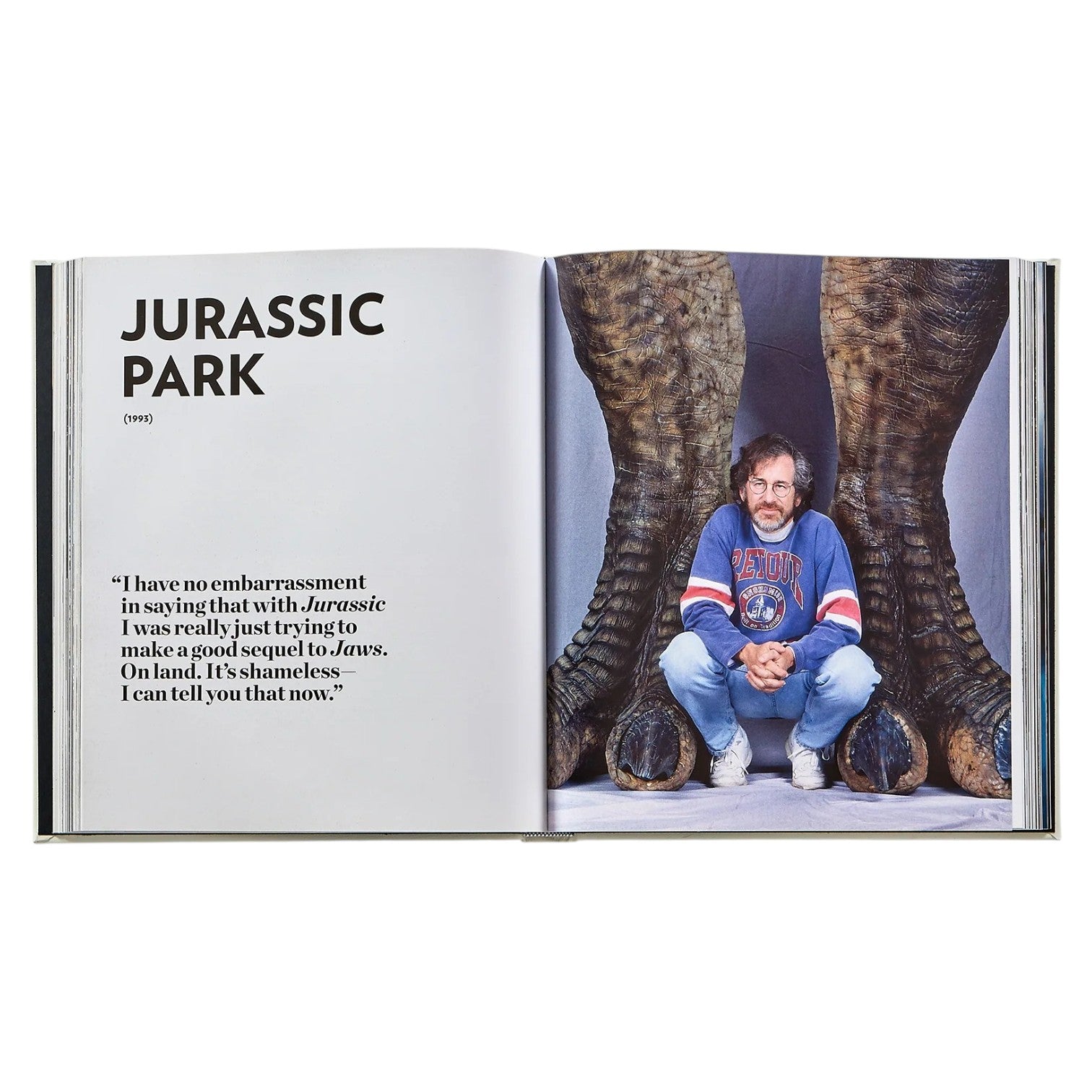 A spread from "Steven Spielberg: A Retrospective" by Graphic Image shows a "Jurassic Park" title, a quote, and a man in a sports jersey crouched between massive dinosaur feet.