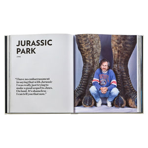 A spread from "Steven Spielberg: A Retrospective" by Graphic Image shows a "Jurassic Park" title, a quote, and a man in a sports jersey crouched between massive dinosaur feet.