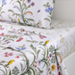 Yves Delorme Botanic Bedding Collection white organic cotton sateen linens featuring a colorful botanical print of meadow flowers, birds, and insects.