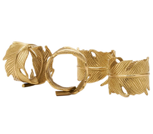 The Neela Napkin Ring Set by Blue Pheasant features four gold brass feather-shaped rings, elegantly displayed together on a white background.