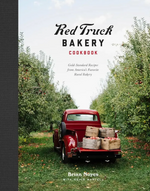 A red vintage truck filled with baskets of apples sits between rows of apple trees, while “Red Truck Bakery Cookbook” by Penguin Random House—featuring delicious southern baking recipes—appears as the title on the book’s cover.