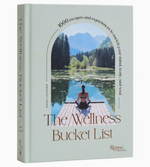 A book titled “The Wellness Bucket List” from the Rizzoli brand features a cover image of a woman meditating by a lake, with mountains and trees in the background, evoking the essence of wellness travel and encouraging readers to prioritize self-care as part of their journeys.