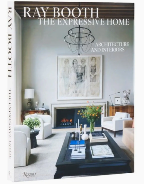Book cover of Ray Booth, The Expressive Home by Rizzoli, featuring a living room with white chairs, a black coffee table, wall art, and a chandelier, evoking the timeless aesthetic of sophisticated homes; includes the subtitle “Architecture and Interiors.”.