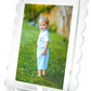 A framed photograph of a young child on green grass in a light blue outfit, with trees and a stone wall behind—displayed in our best-selling Tara Wilson Designs Scallop Frame Collection, which beautifully enhances any cherished memory.