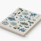 The Riffle Paper Co. Wildwood Embroidered Guest Book is a closed fabric-covered journal featuring blue and green floral embroidery and "Gratitude" stitched on the cover.