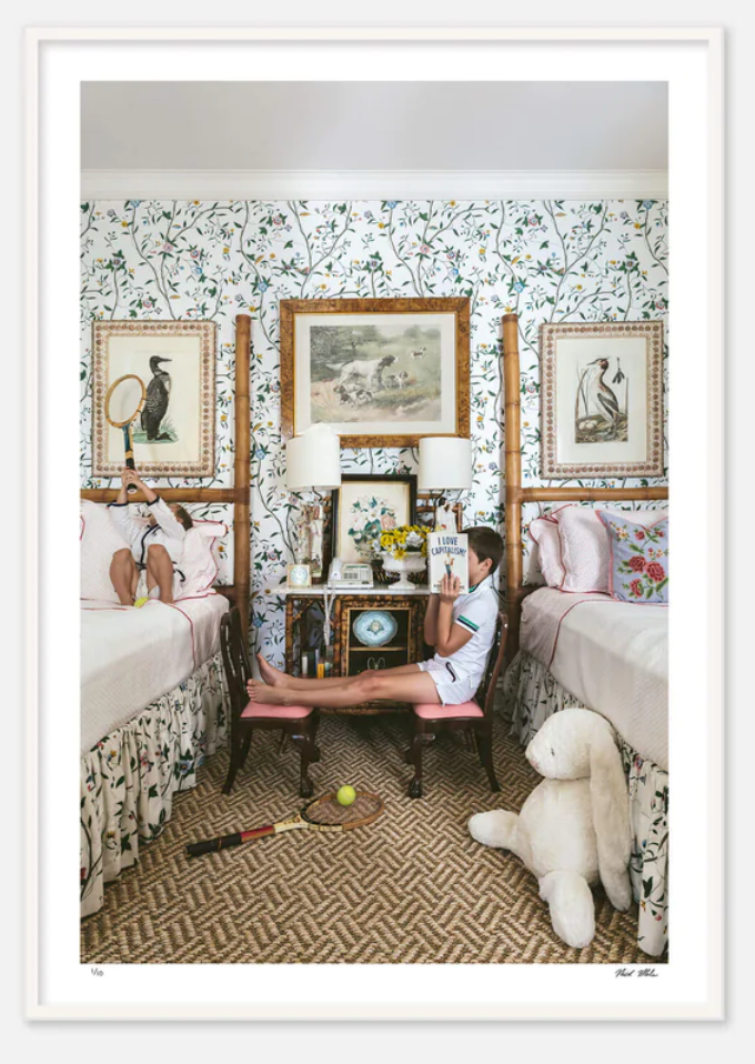 A woman sits on a bench between two twin beds in a Nick Mele Photography location, reading a book, surrounded by plush toys and Nick Mele Fine Art I Love Capitalism.