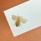 The Printery Bee Place Card Set features bone white cards with an embossed gold bee illustration on a brown background—elegant tented place cards perfect for your special event.
