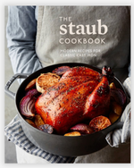 A roasted chicken in a Staub enameled cast-iron pot surrounded by onions and garlic is pictured. The text reads: "The Staub Cookbook: Modern Recipes for Classic Cast Iron" by Penguin Random House.