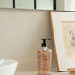 The Baobab Collection Women Body Wellness Collection soap dispenser by Baobab adds a floral touch to the bathroom countertop, set beside a framed sketch and white sink, with a mirror in the background.