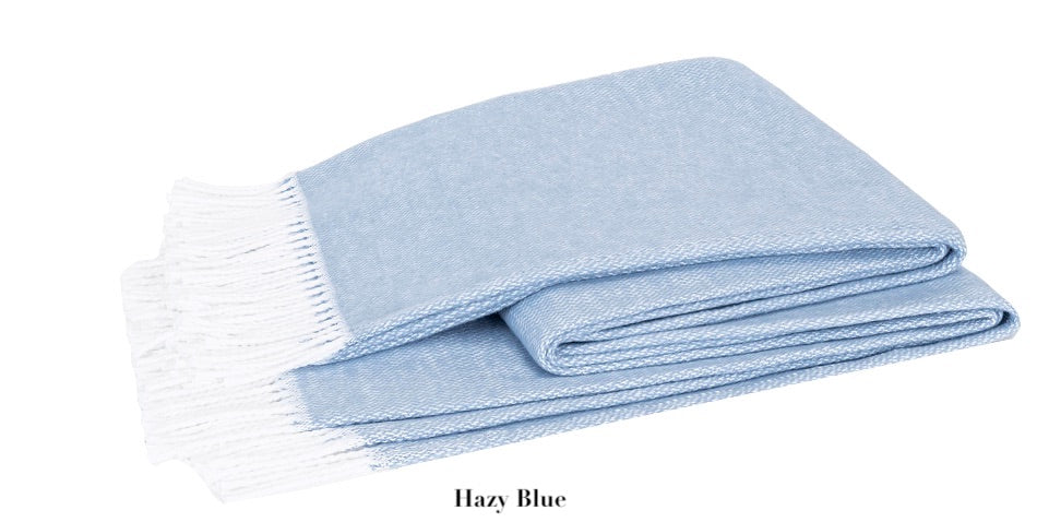 A folded light blue Pezzo Throw from Matouk, featuring white fringed edges and made from OEKO-TEX certified brushed cotton, labeled "Hazy Blue.