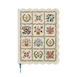 The Helena Softcover Journal by Rifle Paper Co. is a cream-colored journal with scalloped edges and a linen textured cover, featuring a floral pattern of 15 blocks—each showcasing different flower arrangements—and comes complete with a blue ribbon bookmark.