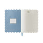 The Helena Softcover Journal by Rifle Paper Co. features an open scallop-edge design, a linen-textured cover, a blue inside cover with a label box, and lined pages each decorated with a small icon at the top.