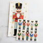 A long Nutcracker Collection napkin and a square napkin featuring ten smaller nutcrackers, both with gold stars, perfect for your holiday table decor.