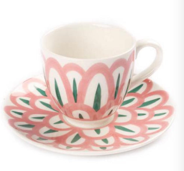 A handcrafted ceramic teacup and saucer from Themis Z's Symi Green and Pink Collection showcase a pink, white, and green floral design.