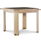 The Willie Oak Game Table by Highland House features a square oak design with four thick legs, gold-colored caps, and horizontal corner protrusions, shown against a white background.