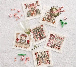 The Kim Seybert Holiday Paws Cocktail Napkin Set includes six embroidered napkins on a snowy surface with glasses, candy canes, and peppermints—a festive holiday accessory and perfect gift for pet lovers.