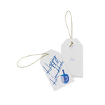 Caspari’s Happy Hanukkah Foil Hanging Gift Tag set includes two high-quality cardstock tags: one with a blue dreidel and “Happy Hanukkah,” the other labeled “To:” and “From:” for a festive, personalized gift presentation.