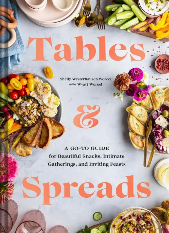Cover of “Tables & Spreads” by Chronicle Books, displaying an artful arrangement of breads, dips, vegetables, fruits, and flowers on a table with the book’s title and subtitle in bold orange text—a comprehensive food styling guide and recipe collection for all occasions.