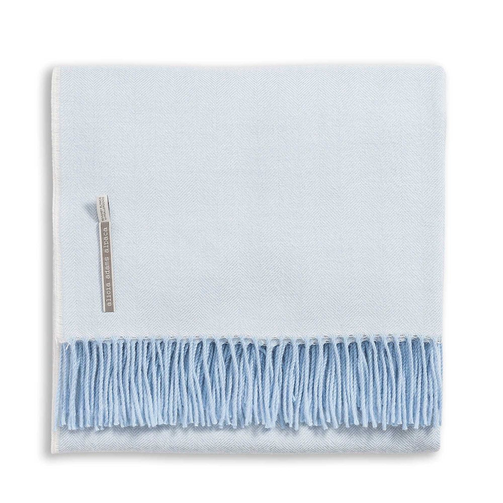 Alicia Adams Alpaca Classic Herringbone Throw, light blue with soft fringe and fabric label, fair-trade made in Peru, displayed folded on a white background.