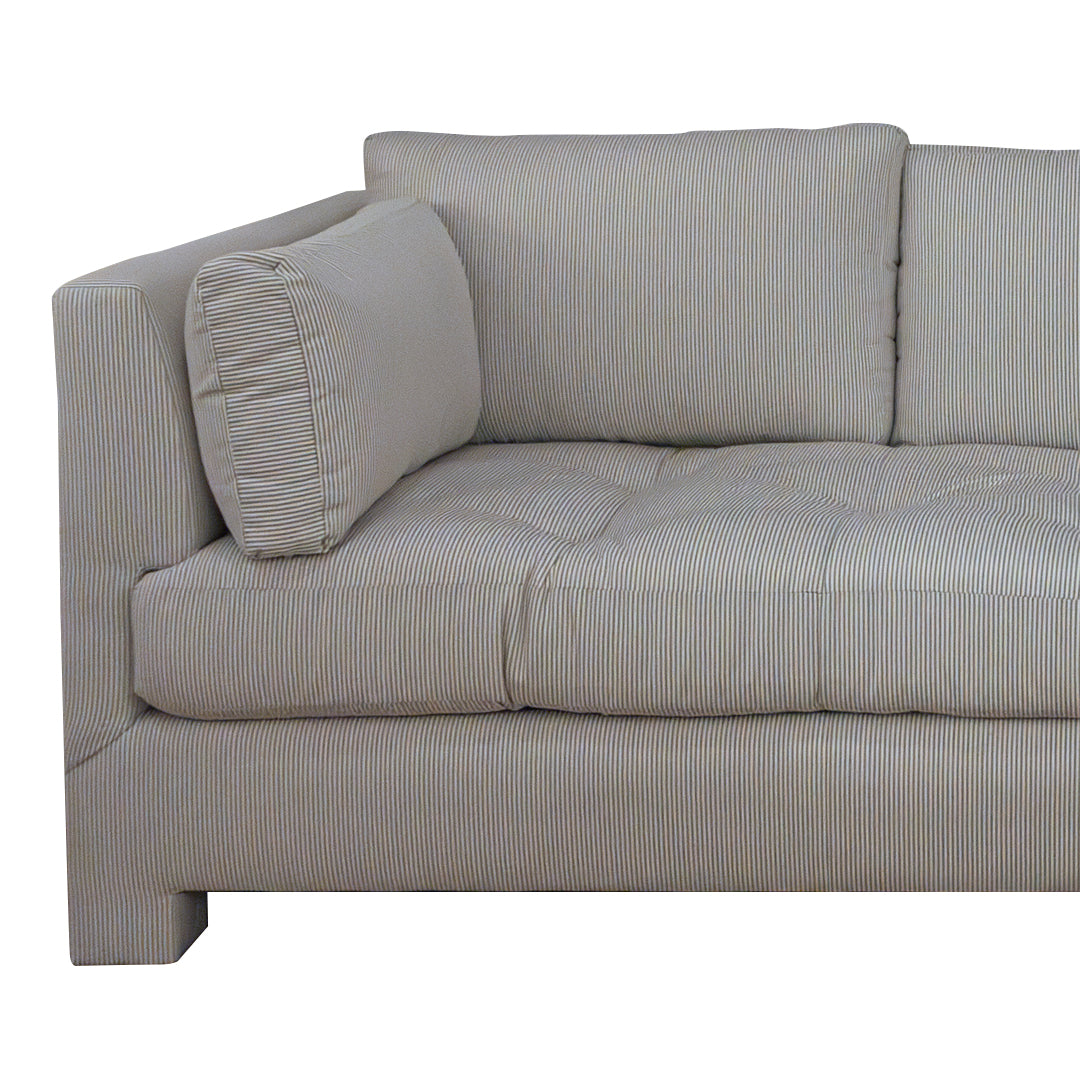 The Barrett Sofa in Ticking Stripe Dove by Highland House features gray and white ticking stripe upholstery, tufted seat cushions, and a matching rectangular pillow for a coastal-inspired look, displayed here from an angled side view.