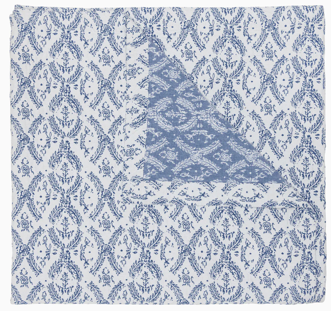 Part of the John Robshaw Aashna Azure Bedding Collection, this square cotton jacquard napkin displays a blue floral and vine motif on white, folded to reveal a contrasting blue design inspired by Portuguese tilework.