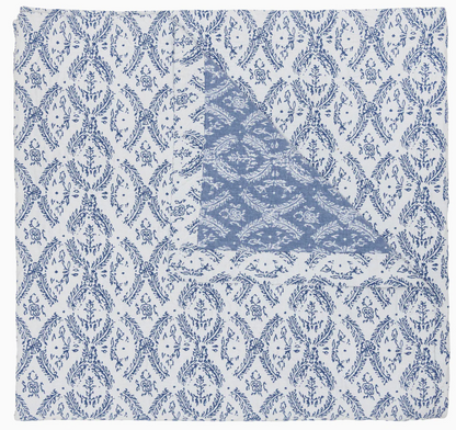 Part of the John Robshaw Aashna Azure Bedding Collection, this square cotton jacquard napkin displays a blue floral and vine motif on white, folded to reveal a contrasting blue design inspired by Portuguese tilework.