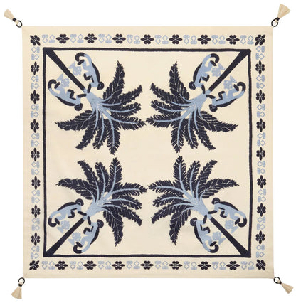 The Ikat Amazónico Napkins by Johanna Ortiz feature a cream background, blue and navy palm tree motifs, a decorative border, and tassels—perfect for adding tropical chic elegance to your table setting.