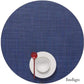 A red spoon, white saucer, and empty cup are arranged on a Chilewich round placemat from the Round Placemat Collection, crafted with phthalate-free Terrastrand yarns.