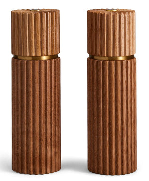 The L'Objet Ionic Salt and Pepper Mill Set features two cylindrical, ribbed European oak mills with brass accents, each equipped with a durable metal grinder, shown standing upright side by side against a white background.