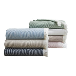 Six Leo Throw blankets by Matouk—crafted from 100% cotton in green, white, blue, beige, pink, and black—are folded and stacked in two piles with fringed edges. Contemporary style meets cozy elegance against a white background.