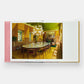 The open book, "Italian Interiors: Rooms with a View" by Phaidon, showcases a captivating photo of a dining room that embodies Italian interior design, complete with a long table surrounded by brown chairs, an elegant chandelier, and a striking green ceiling.
