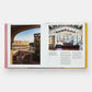 The opened pages of "Italian Interiors: Rooms with a View" by Phaidon reveal a breathtaking penthouse balcony view beside a roomy living area characterized by wooden beams and expansive windows, epitomizing the sophistication often associated with Italian interior design.
