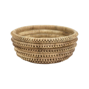 The Kenis Braided Bowl by PALECEK is a round, hand-woven rattan bowl with a natural finish, horizontal ridges, and a flat base, crafted from natural materials and shown on a white background.