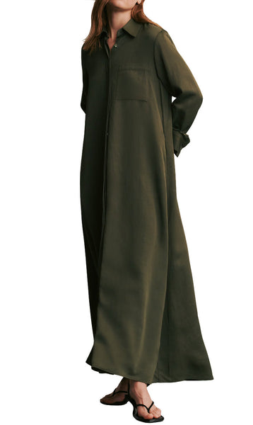 Woman modeling a long sleeve olive green TWP Jennys Gown made of coated viscose linen, featuring a collar and button-down front, paired with black flats. Care instruction: dry clean only.