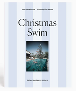 The Piecework Slim Aarons Puzzle Collection includes a 1000-piece jigsaw puzzle featuring “Christmas Swim,” showcasing a vibrant photograph of a swimmer in a pool with a Christmas tree beneath a bright sky. Crafted from high-quality art paper and recycled paper, this puzzle combines beauty with eco-friendly materials.
