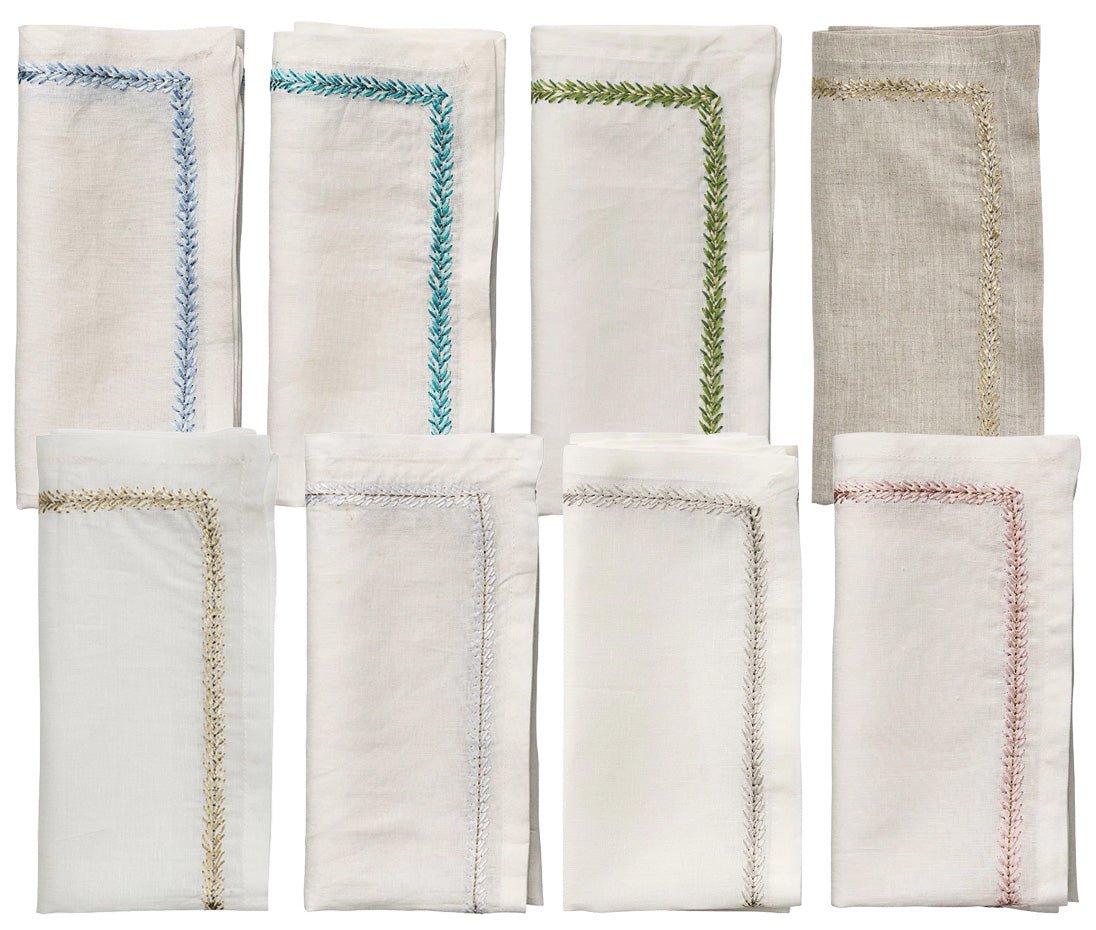 The Kim Seybert Jardin Napkin Set includes eight folded linen napkins, each with a unique embroidery border in neutral tones, arranged in two rows on a white background.