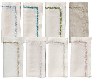 The Kim Seybert Jardin Napkin Set includes eight folded linen napkins, each with a unique embroidery border in neutral tones, arranged in two rows on a white background.