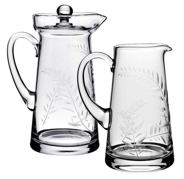 Two cherished pitchers from the William Yeoward Crystal Jasmine Pitcher Collection, crafted from clear glass and featuring handles with etched leaf designs in the Jasmine Cutting style. One includes a lid, making them an ideal wedding present from William Yeoward Crystal.