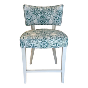 The A. Rudin Counter Stool in Turquoise Shell Grato features white wooden legs and a padded seat and backrest upholstered in green and white grato fabric with an intricate seashell and coral motif.