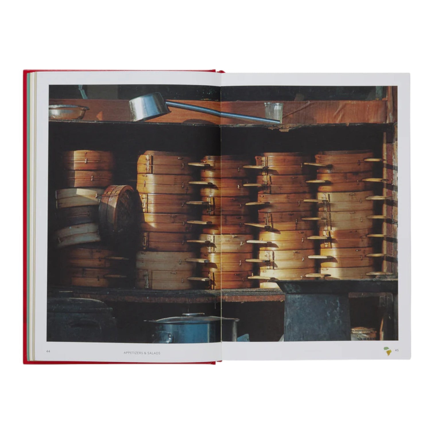 China: The Cookbook by Phaidon sits on a kitchen shelf among wooden steamers, metal pots, and utensils—offering the perfect guide for mastering authentic Chinese recipes.