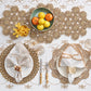 A stylish tablescape with two place settings, gold-trimmed napkins, cutlery, crystal glasses, citrus fruit bowl, and snacks on the Kim Seybert Embroidered Palm Tablecloth adds chic desert flair.